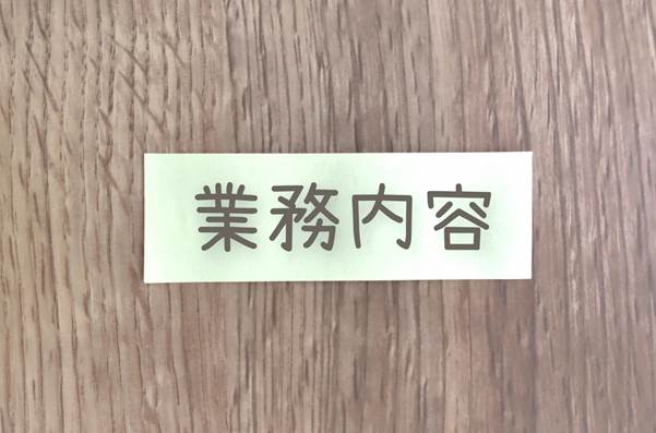 “業務内容”と書かれた紙が木目の背景に貼られている