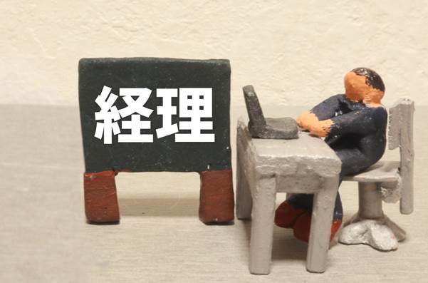 “経理”と書かれた黒板のそばで、パソコンを使う人物